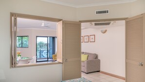 Un dormitorio con cama, ventana, puerta corredera, ventilador de techo y vistas a un balcón con mobiliario exterior.