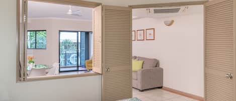 Un dormitorio con cama, ventana, puerta corredera, ventilador de techo y vistas a un balcón con mobiliario exterior.