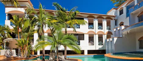 A resort with a swimming pool, palm trees, and a multi-story building with balconies.
