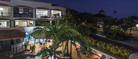 A multi-story hotel with a pool, outdoor seating, and palm trees.