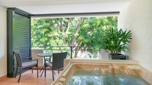 Un balcón con un jacuzzi, una silla, una mesa y una planta en maceta.