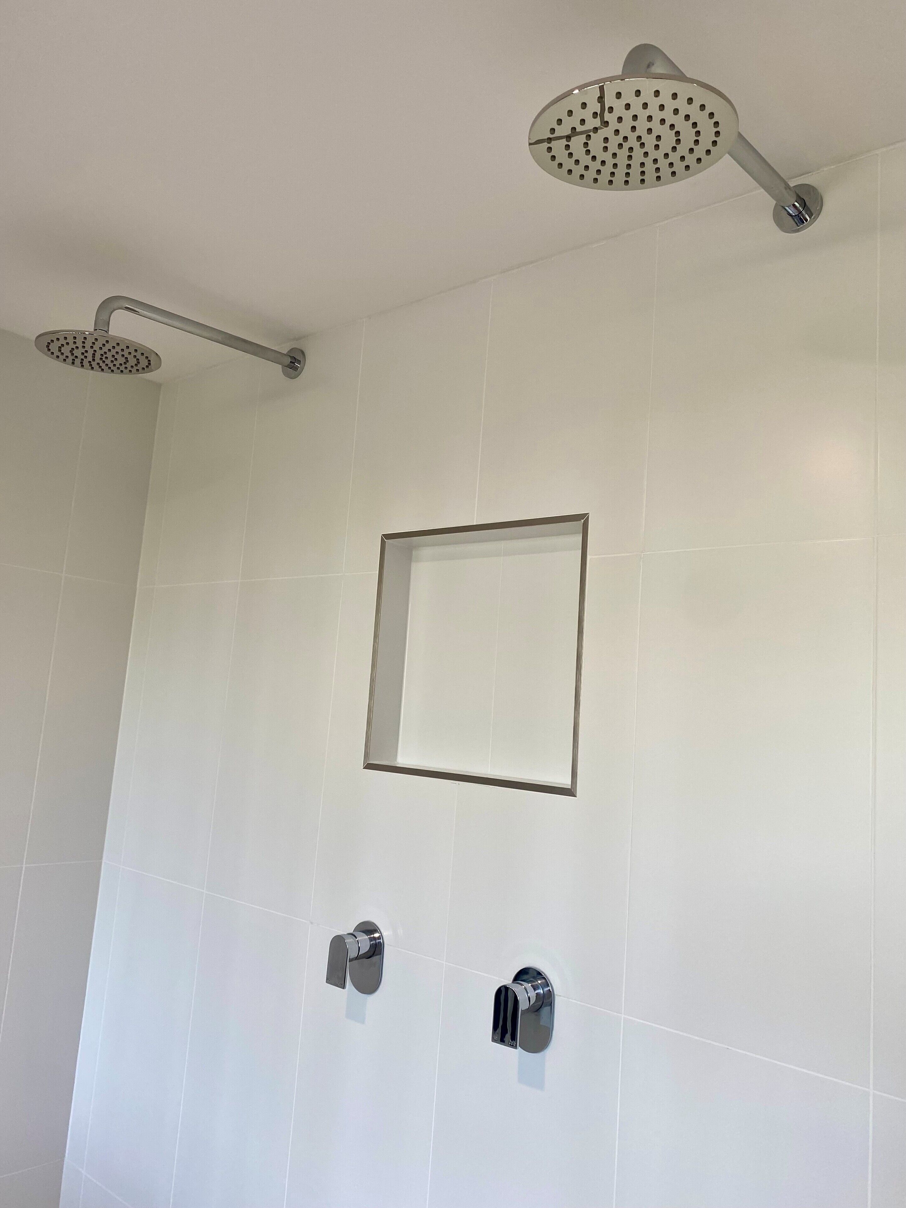 A bathroom with white tiles, a showerhead, and two faucets.