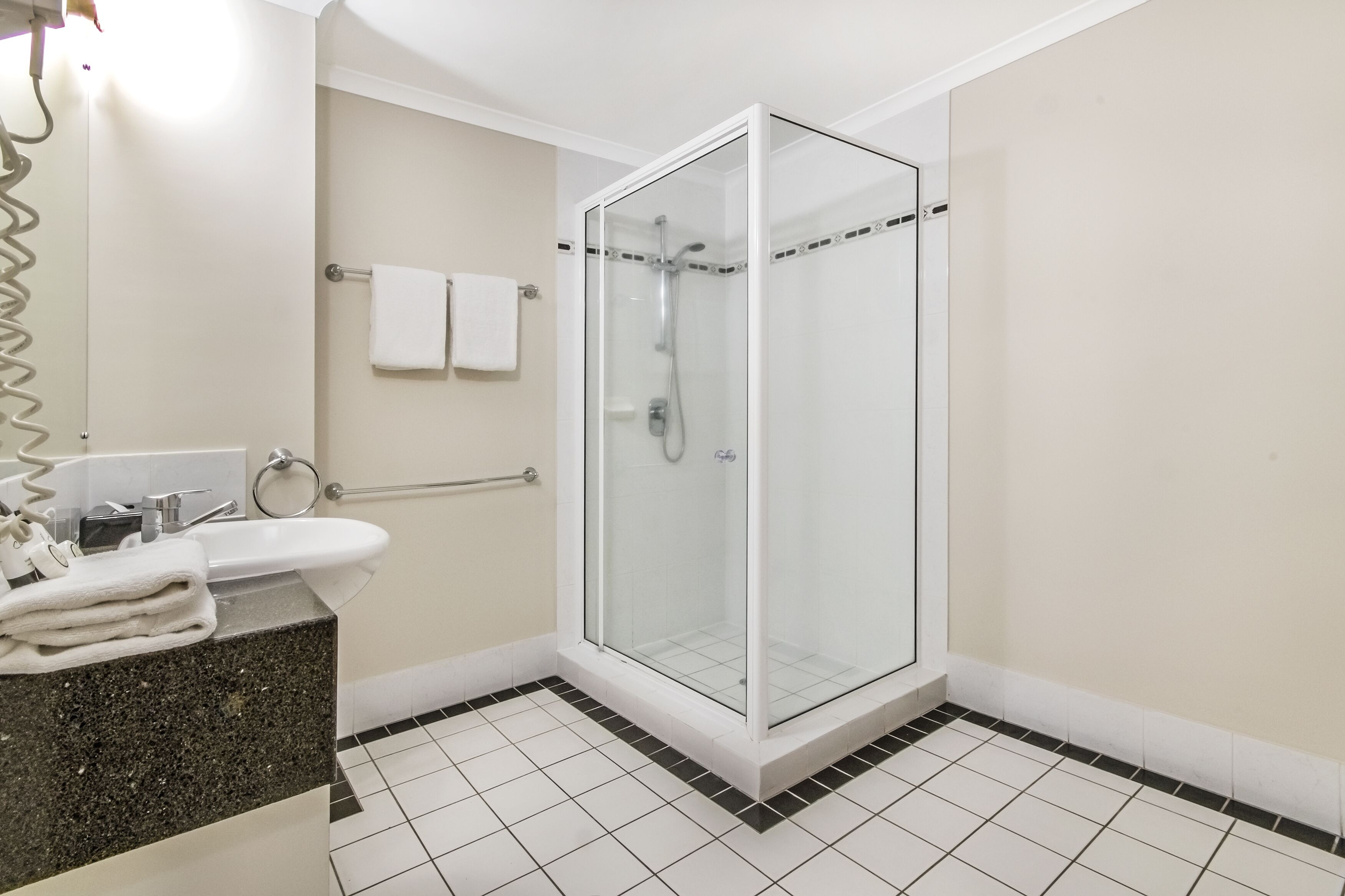 Un baño moderno con ducha de vidrio, lavamanos blanco y piso de baldosas.