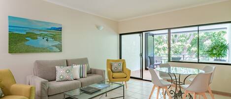 A modern living room with a glass coffee table, a sofa, a yellow armchair, and a dining table with chairs.