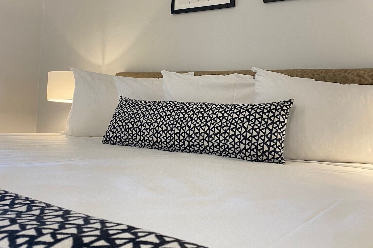 Une chambre d’hôtel avec un lit soigneusement fait, un plaid à motifs et deux œuvres d’art encadrées accrochées au mur.