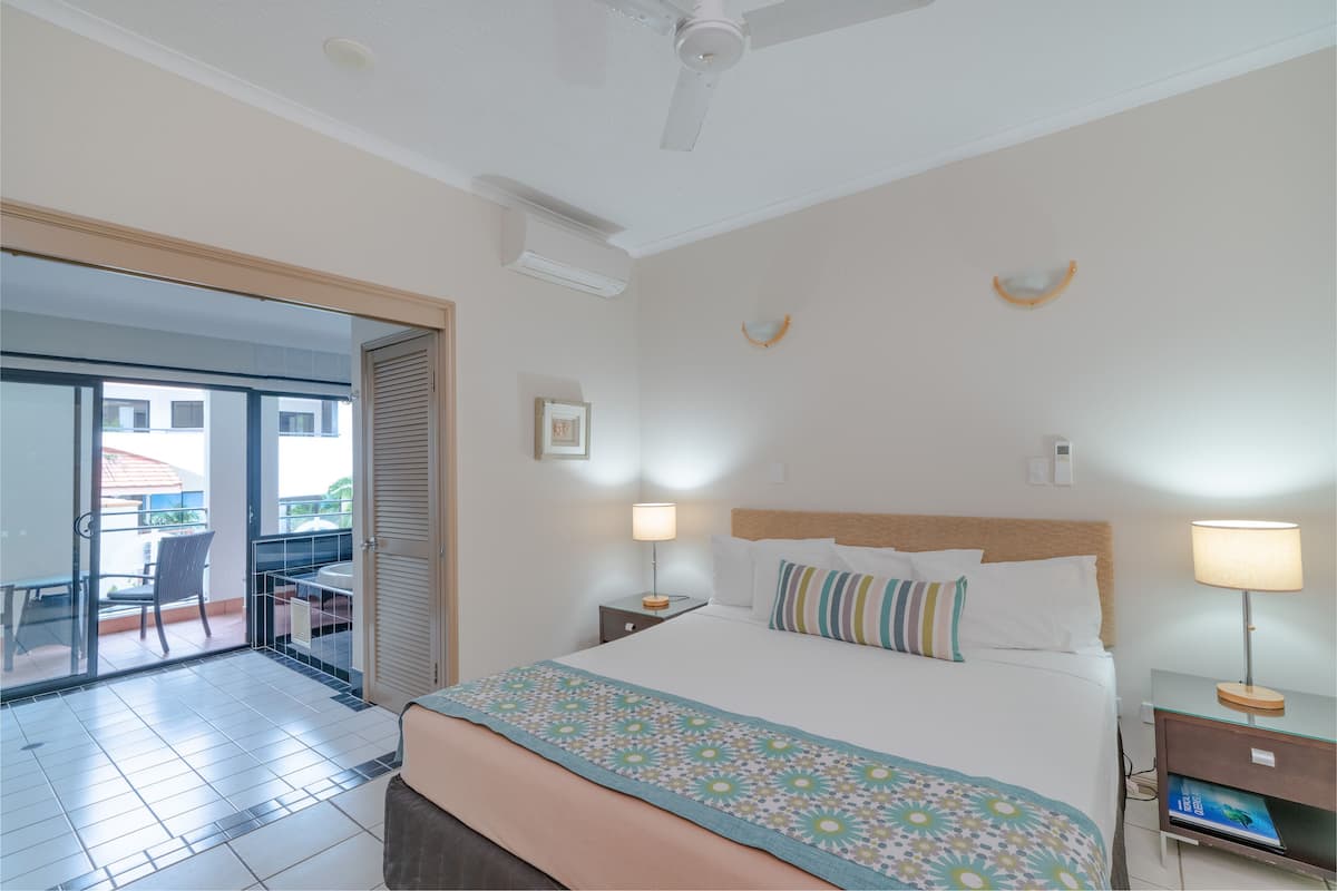 Une chambre d’hôtel avec un lit, une table de chevet, une lampe, une chaise et un balcon avec vue.