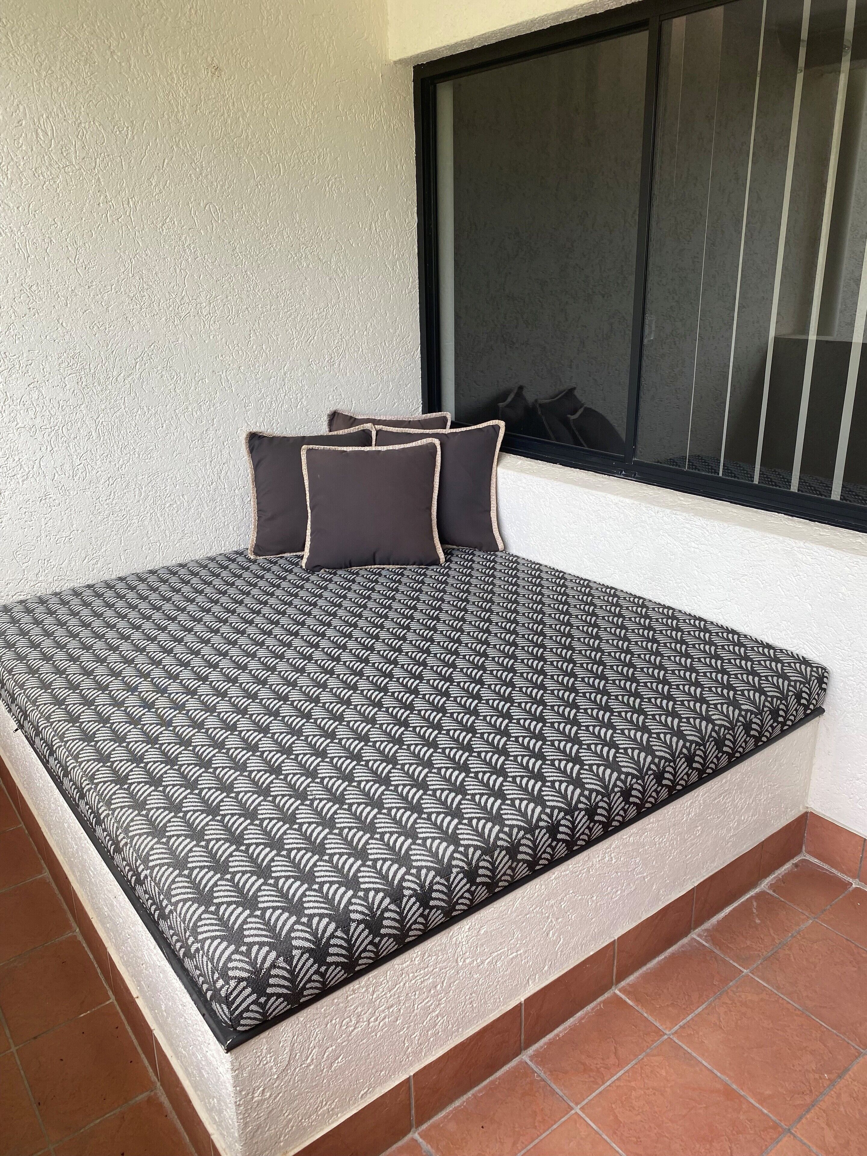 Un lit avec une couvre-lit à motifs et deux oreillers, une fenêtre avec des stores et un sol carrelé.