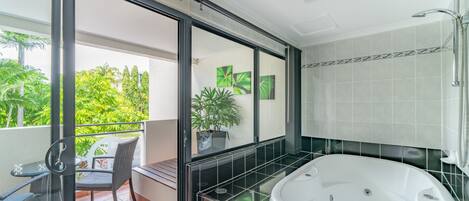 A modern bathroom with a large bathtub, a glass-enclosed balcony with outdoor furniture, and a view of greenery.