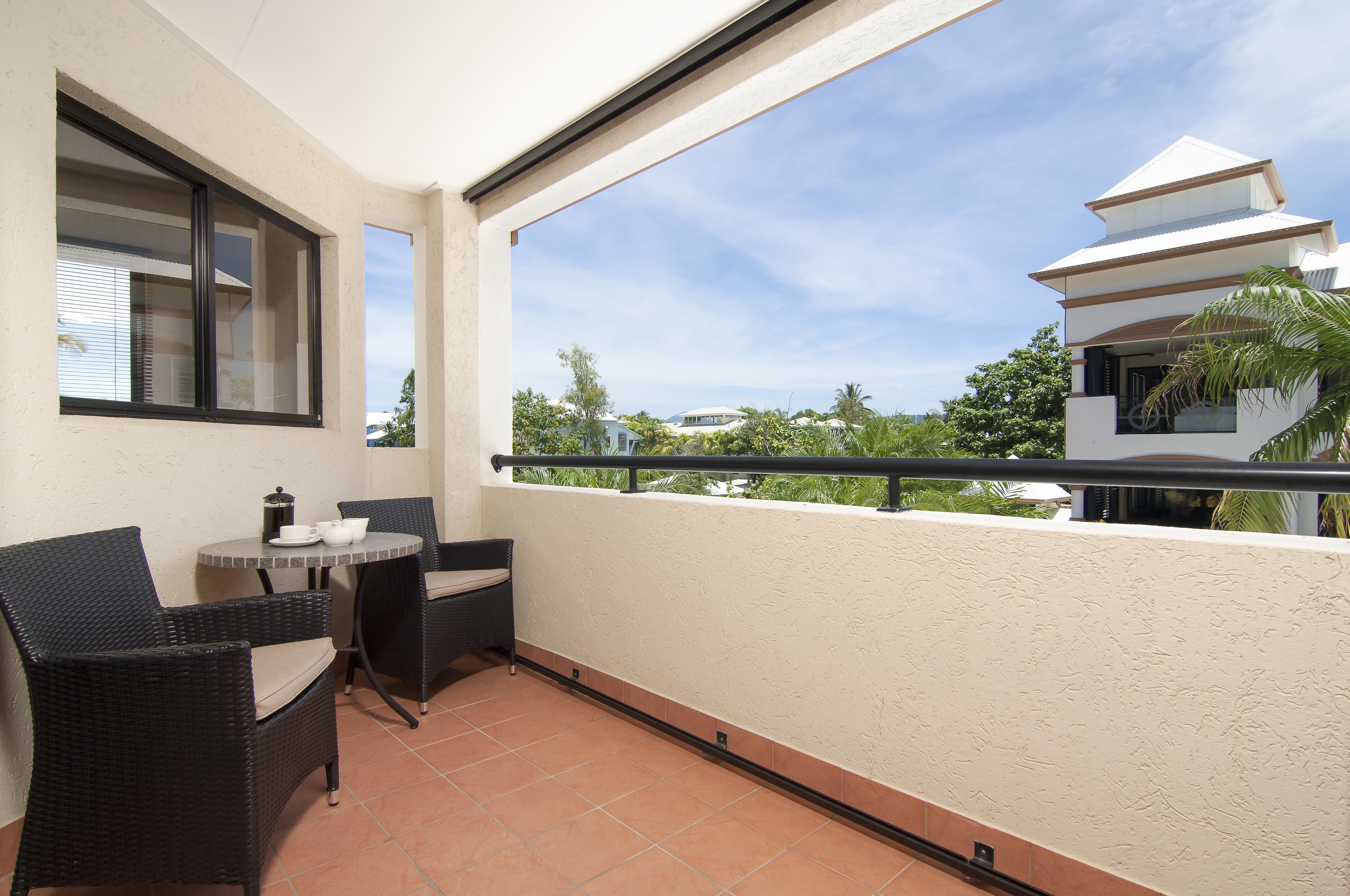 A balcony with a table and chairs, a view of a modern building, and a clear sky.