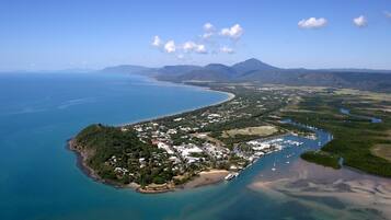 Vista aérea de un pueblo costero con playa, puerto deportivo y vegetación circundante.