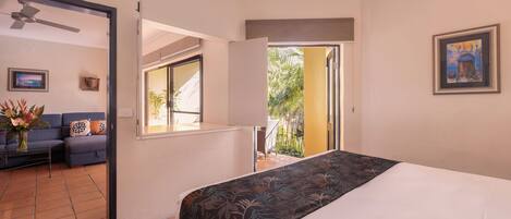 A hotel room with a bed, a sofa, a ceiling fan, a window, and a door leading to an outdoor area.