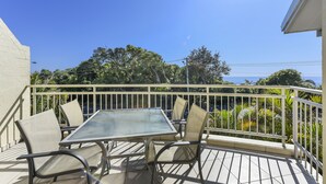 An outdoor patio with a table and chairs, a white railing, and a view of trees and the ocean. - Flynns Beach Resort (Port Macquarie)