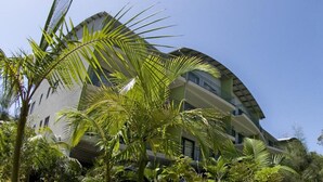 A modern hotel with a curved facade, multiple balconies, and lush tropical vegetation. - Flynns Beach Resort (Port Macquarie)
