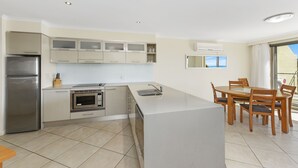 A modern kitchen with a built-in oven, microwave, and refrigerator. There is a dining area with a table and chairs. - Flynns Beach Resort (Port Macquarie)