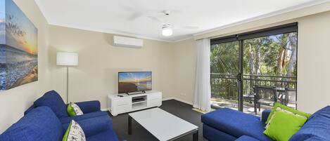 A modern living room with blue sofas, a white coffee table, and a flat-screen TV on a white cabinet.