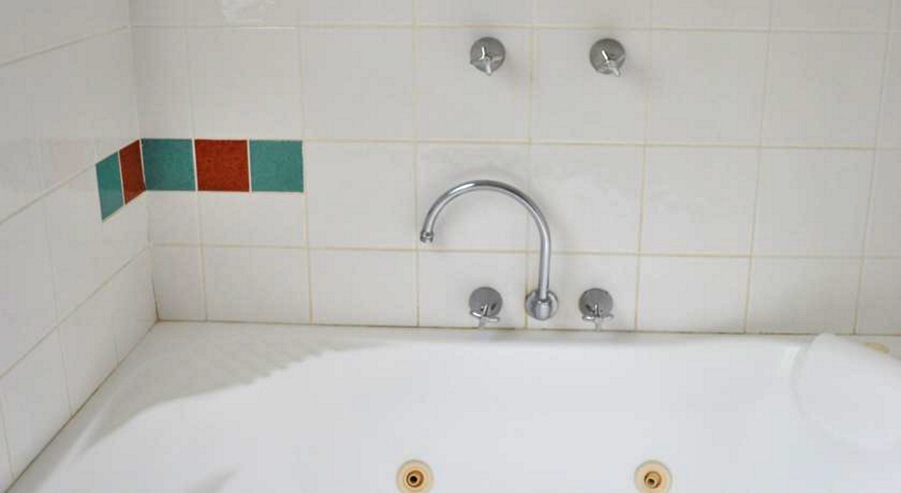 A bathroom with a white bathtub, two faucets, and a single showerhead.