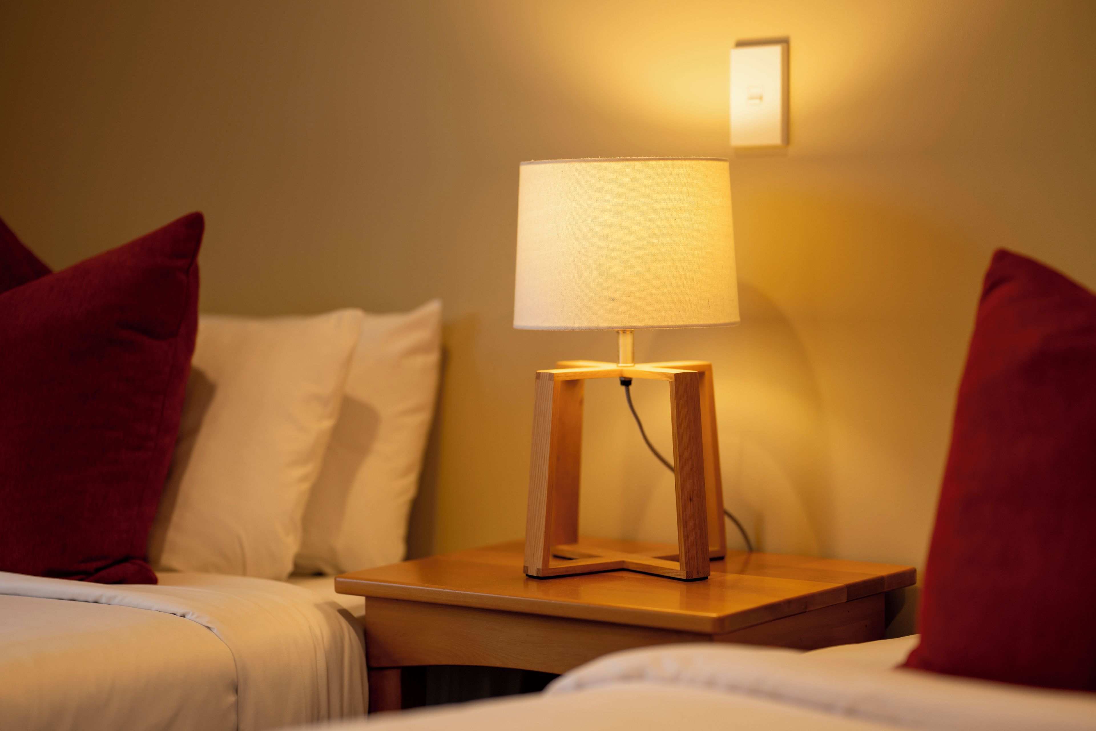 A hotel room with a bedside table, a lamp, and two beds with pillows.