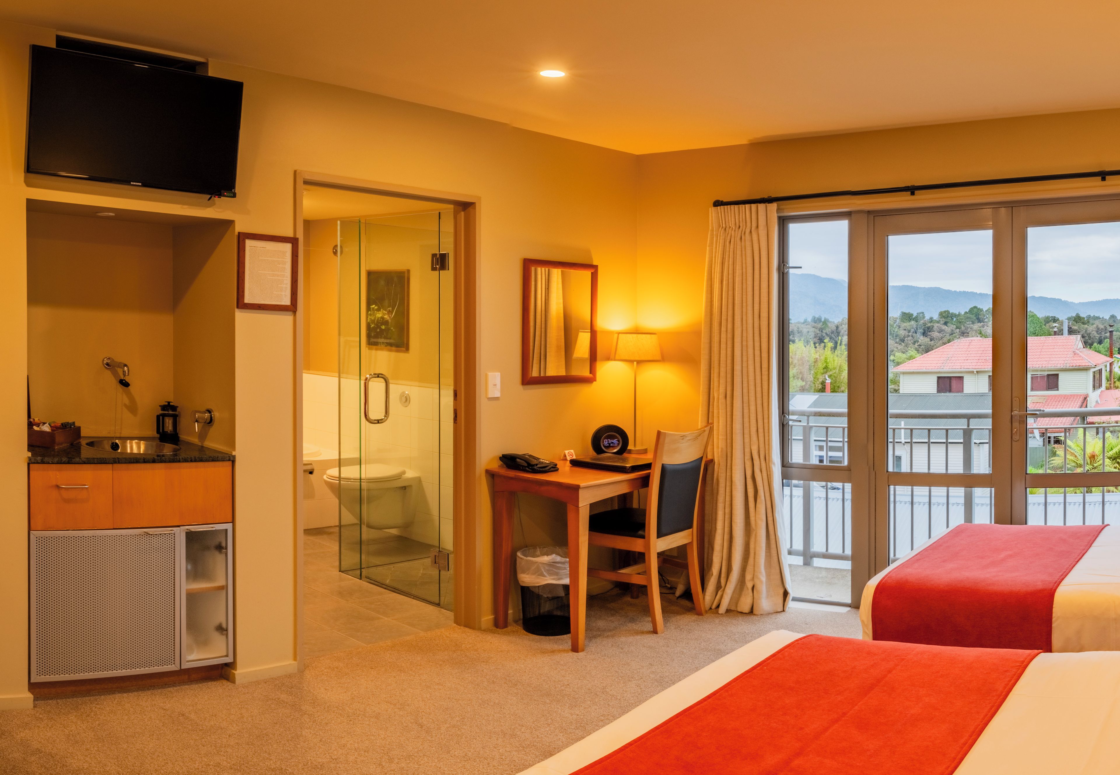 A hotel room with a bed, a desk, a chair, a television, a bathroom, and a view of the outside.