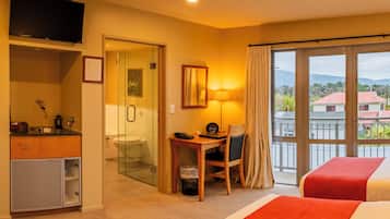 A hotel room with a bed, a desk, a chair, a television, a bathroom, and a view of the outside.