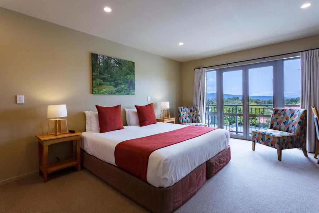 A hotel room with a large bed, two bedside tables with lamps, a colorful armchair, and a balcony with a view.