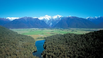 A mountainous landscape with a river, dense forests, and snow-capped peaks.
