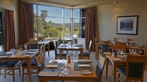 A dining area with tables set for four, large windows offering a view of the outdoors, and a framed picture on the wall. - Te Weheka Hotel Fox Glacier  (Fox Glacier)