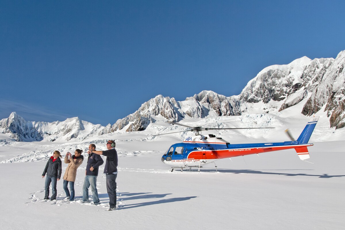 Un hélicoptère portant l’inscription « HELICOPTER UNEC » est stationné sur la neige.