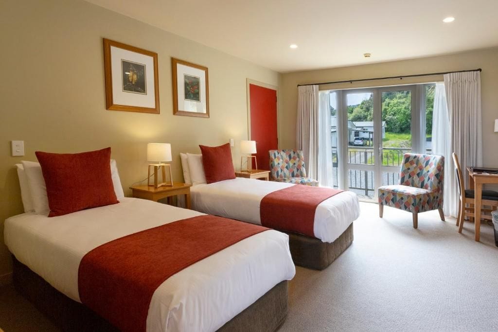 A hotel room with two beds, a chair, a desk, and a balcony with a view.