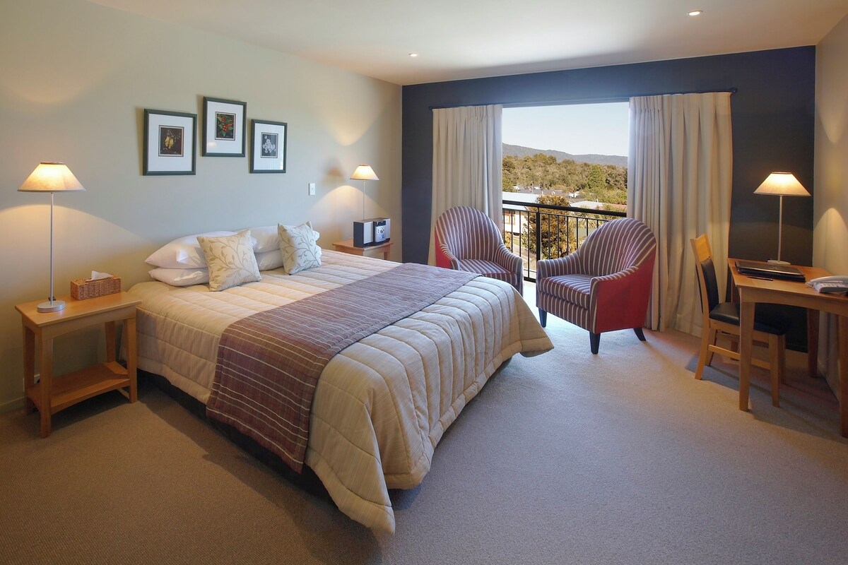 Habitación de hotel con una cama grande, dos sillas, un escritorio y un balcón con vistas.