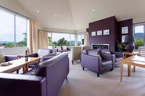 Une chambre d’hôtel moderne dotée d’une grande fenêtre, d’une cheminée et d’un coin salon avec des canapés et des fauteuils.