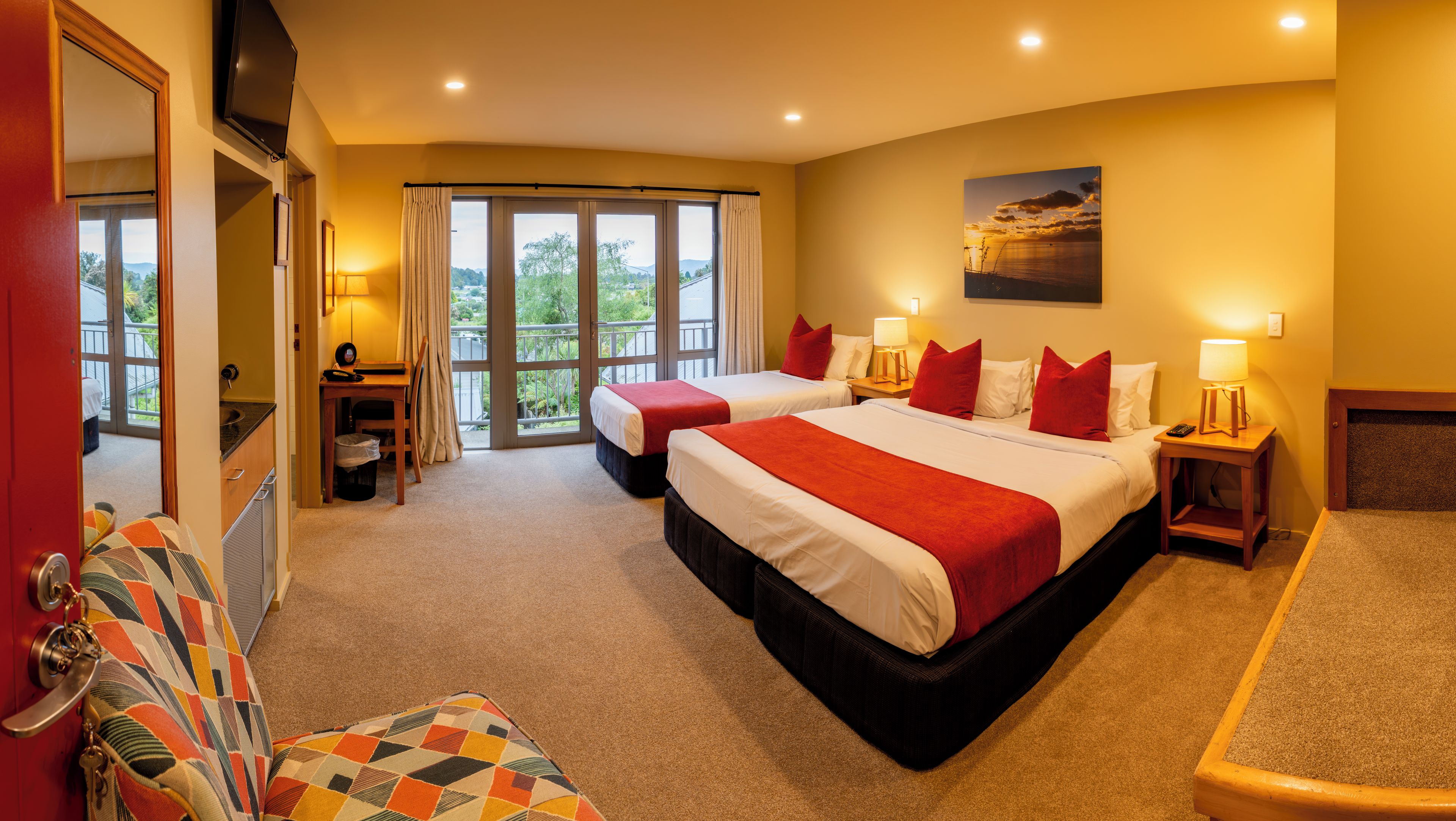 A hotel room with two beds, a desk, a chair, and a view of the outdoors.