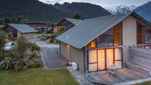 A modern cabin with a large deck, a covered outdoor seating area, and a view of mountains in the background.