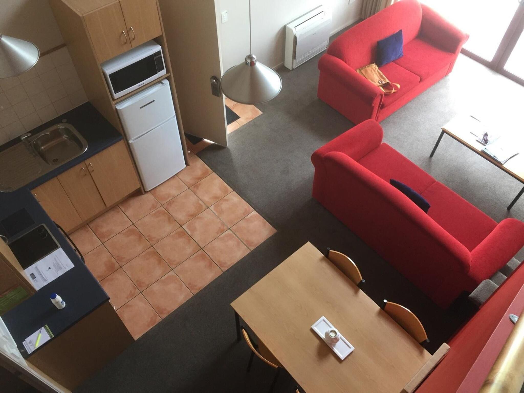 Ein gemütlicher Wohnraum mit Küchenzeile, einem roten Sofa, einem kleinen Esstisch und Blick durch ein Fenster.