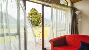 A red sofa with a blue pillow in a room with a sliding glass door leading to an outdoor area with a table and chairs.