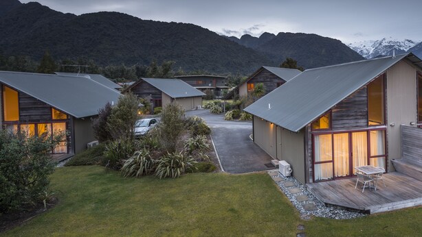 A modern cabin-style hotel with a large deck and a mountain backdrop.