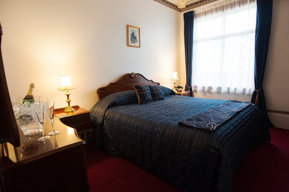 A hotel room with a large bed, two bedside tables with lamps, a framed picture on the wall, and a window with curtains.