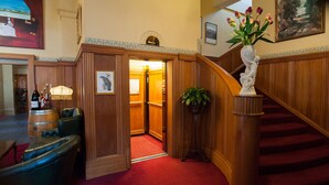 A lobby with a red carpet, wooden paneling, a staircase, a bar area with a lamp, and a vase with flowers.