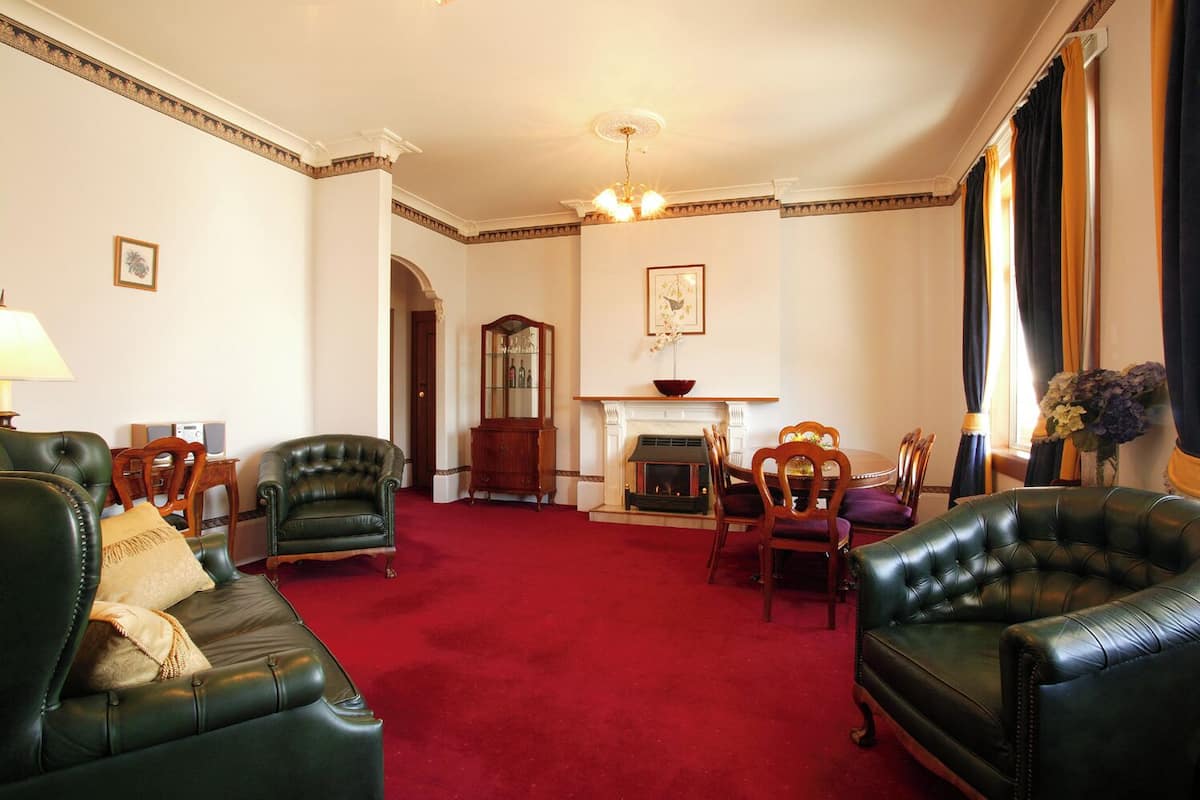 A spacious living room with a red carpet, leather armchairs, a fireplace, and a dining area with wooden furniture.