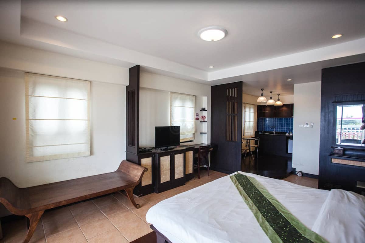 Une chambre d’hôtel comprenant un lit, un bureau avec un ordinateur, une chaise, une fenêtre et un coin cuisine.