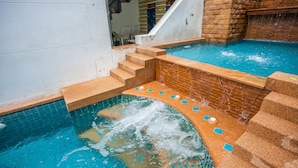 Een zwembad met een kleine waterval, een trap die in het water leidt en een bakstenen muur.