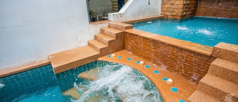 Una piscina con una pequeña cascada, escalones de acceso al agua y un muro de ladrillo.