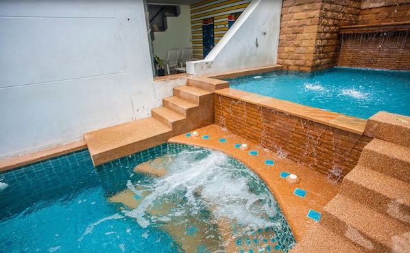 Uma piscina com uma pequena cascata, degraus para entrar na água e uma parede de tijolos.