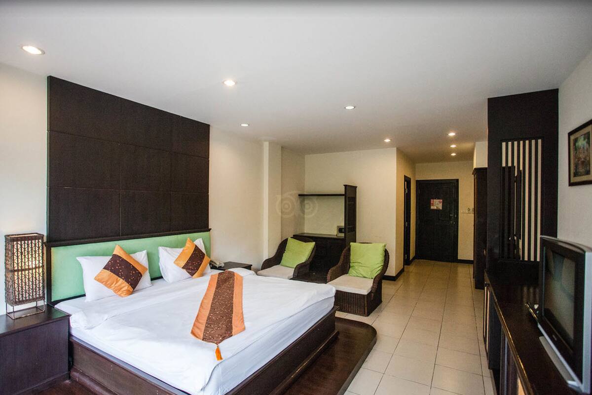 Une chambre d’hôtel avec un grand lit, deux fauteuils, une télévision et un bureau.