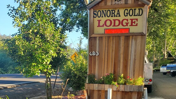 A wooden sign for Sonora Gold Lodge with a 'VACANCY' label, surrounded by a garden with rocks and plants. - Sonora Gold Lodge (Sonora)
