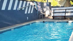 A swimming pool with clear blue water, a fence with a blue and white striped pattern, and a bench with a perforated design. - Sonora Gold Lodge (Sonora)