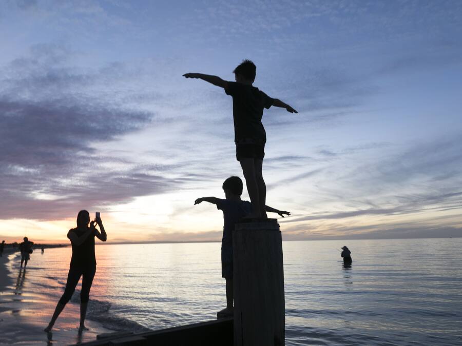 Escena de playa con un poste de madera y una estatua de una persona sobre él.