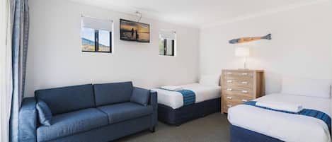 Une chambre d’hôtel avec un canapé bleu, un lit recouvert d’une courtepointe bleue et blanche, une commode en bois et deux téléviseurs fixés au mur diffusant une scène de coucher de soleil.