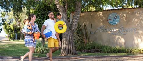 A family walking past a wall with a logo and the text "Aguari Resort".