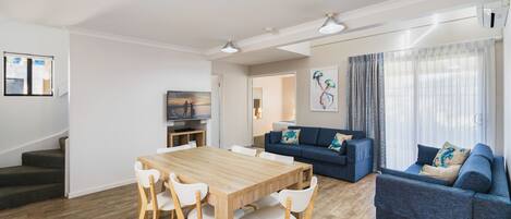 Uma sala de estar moderna com uma mesa de jantar de madeira, cadeiras brancas, um sofá azul e uma escada.
