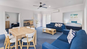 A modern living room with a wooden dining table, blue sofas, and a ceiling fan.
